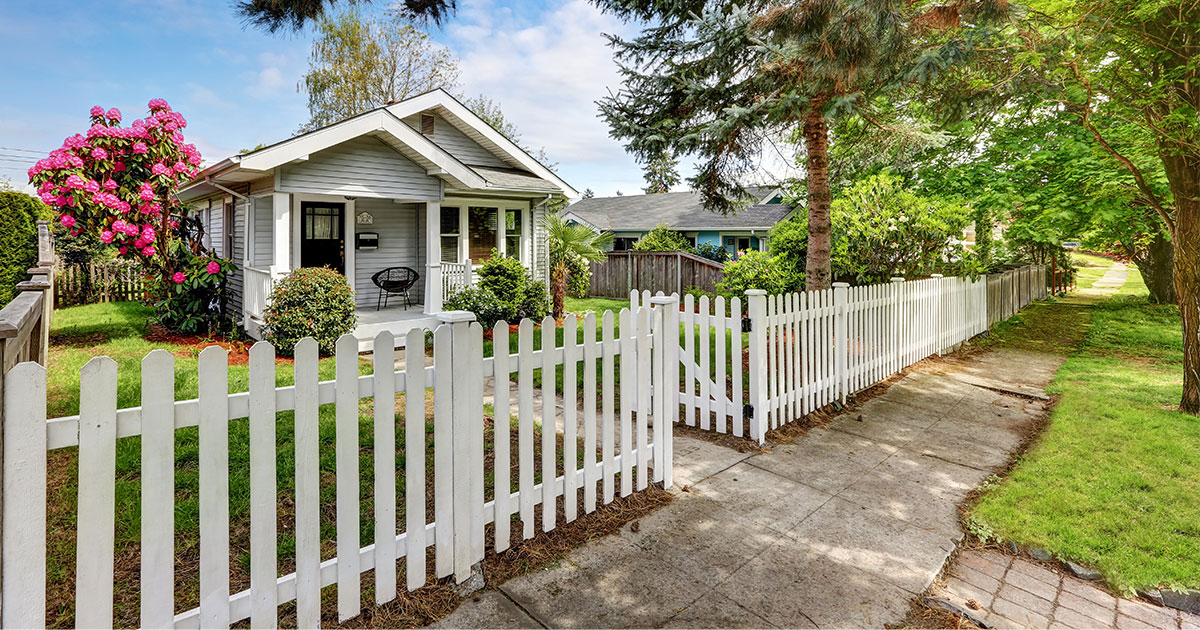 A picket fence made of vinyl with small home and patch of grass